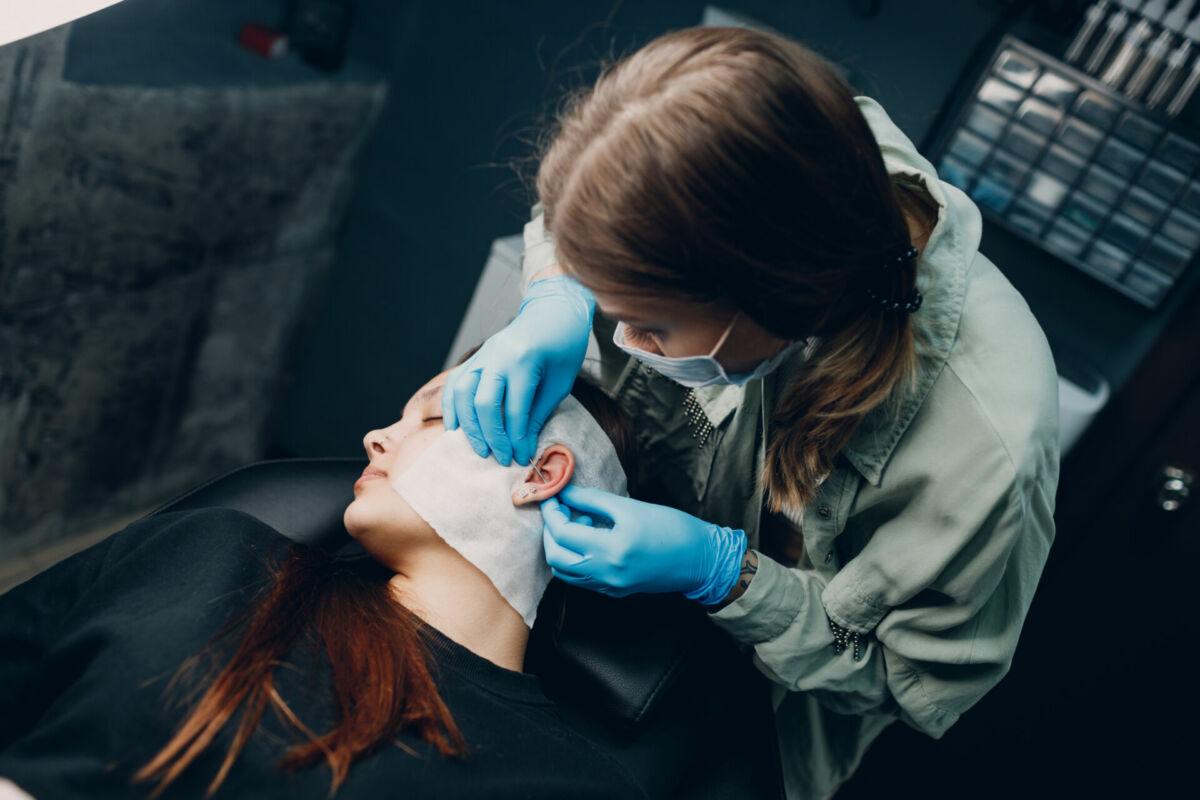 A piercer wearing blue gloves carefully performing an ear piercing on a client