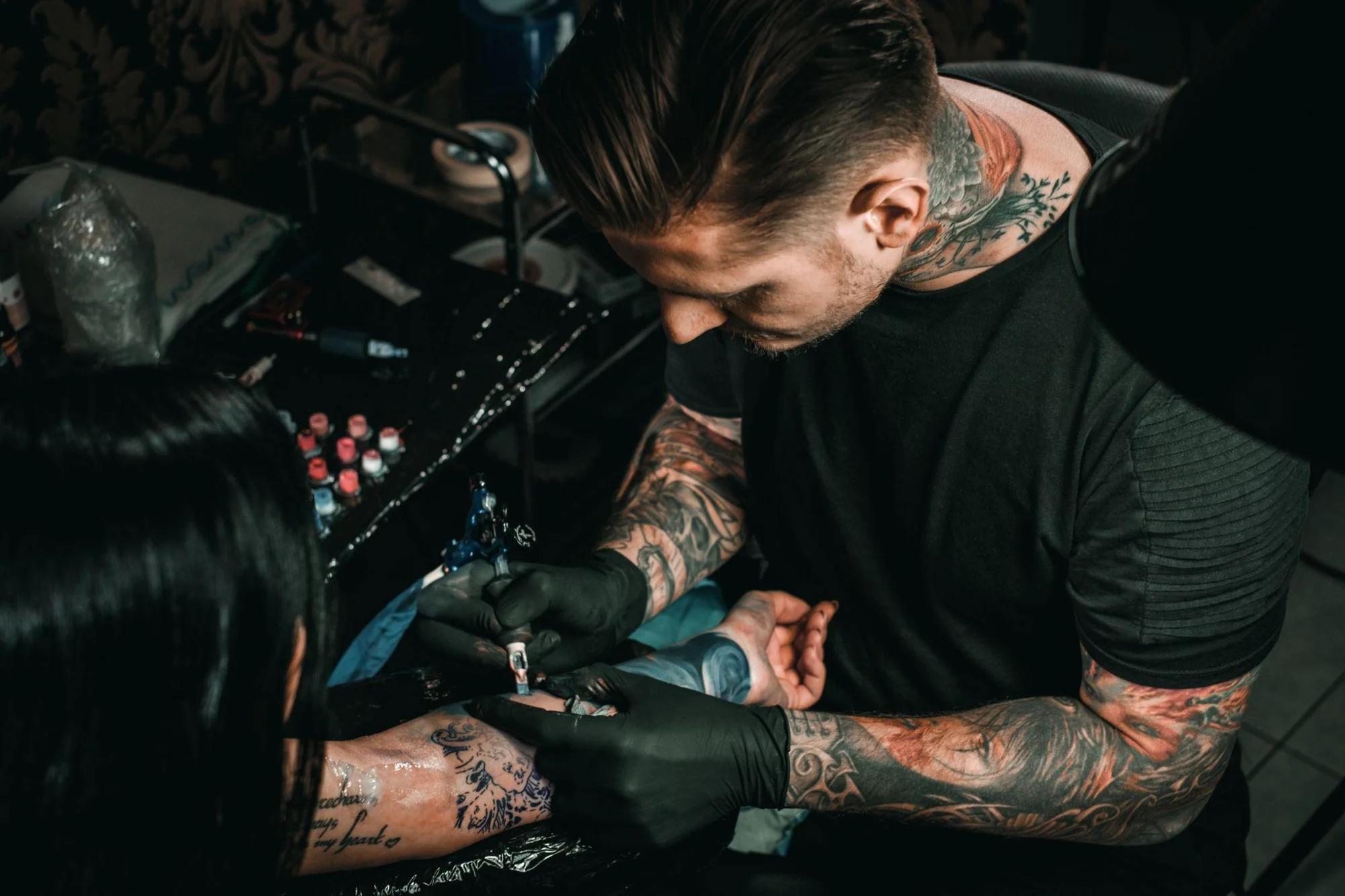 A tattoo artist at work, tattooing a detailed design on a client's forearm
